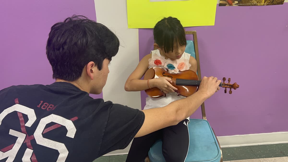 An OCAPEX mentor guiding a young child&rsquo;s hands on the violin