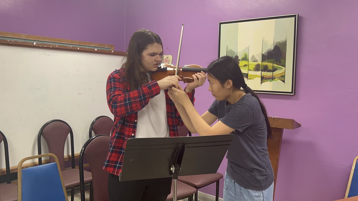 An older OCAPEX student demonstrating a violin passage for a younger musician