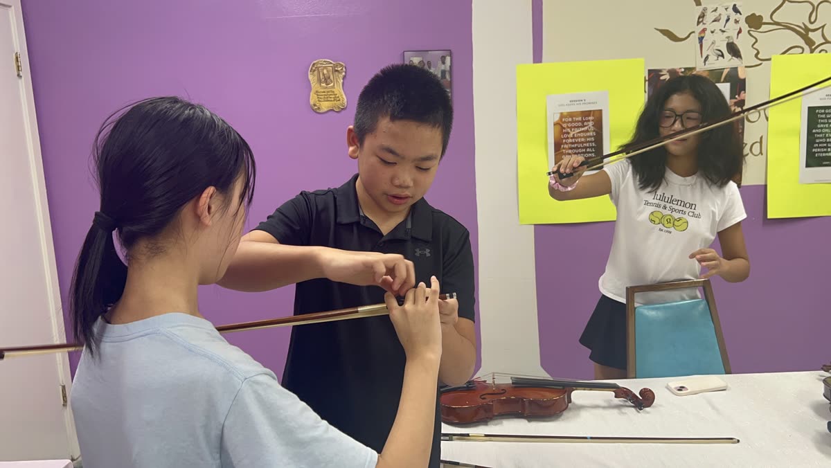 An OCAPEX mentor adjusting a younger student&rsquo;s bow hold