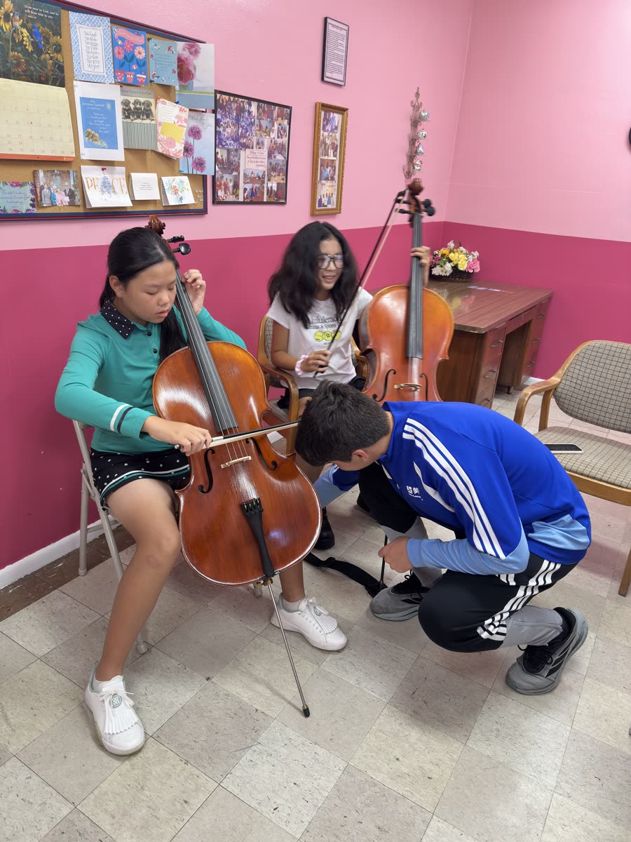 An OCAPEX mentor kneeling to help a young cellist with her setup