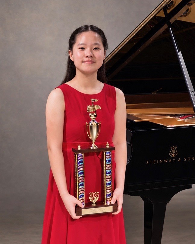 Christina Koyama holding a trophy in front of a grand piano